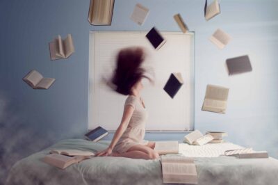 woman on bed with books flying around