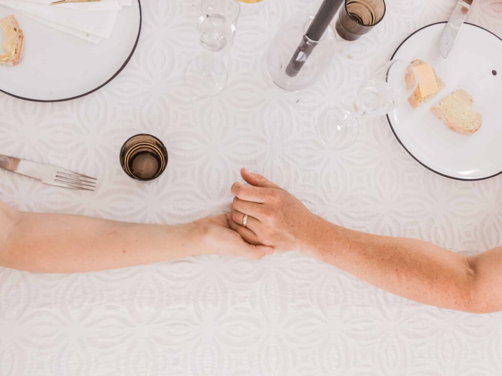 two people holding hands on a table with place settings