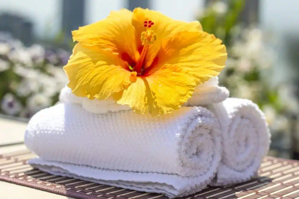 two white towels rolled up beneath a yellow flower